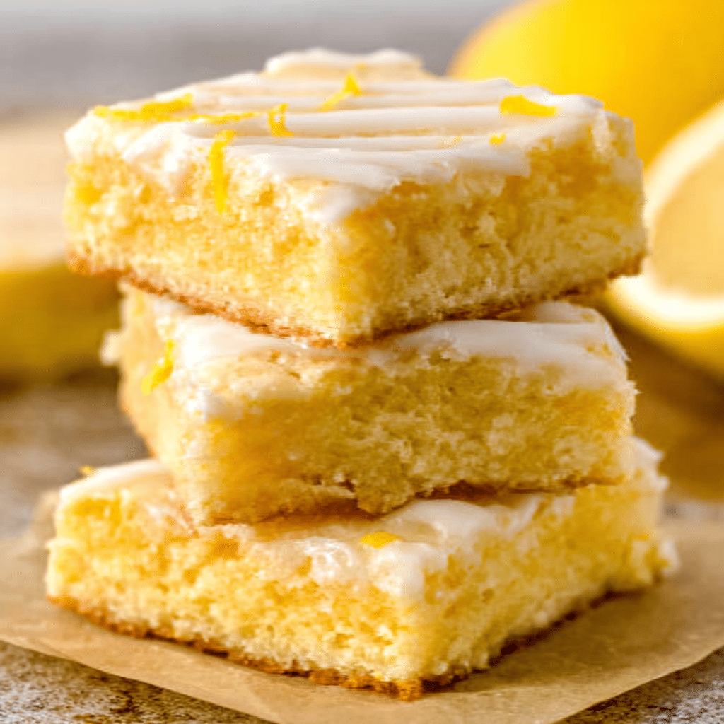 Close-up of lemon brownie bars squares topped with lemon icing and zest, surrounded by lemons.